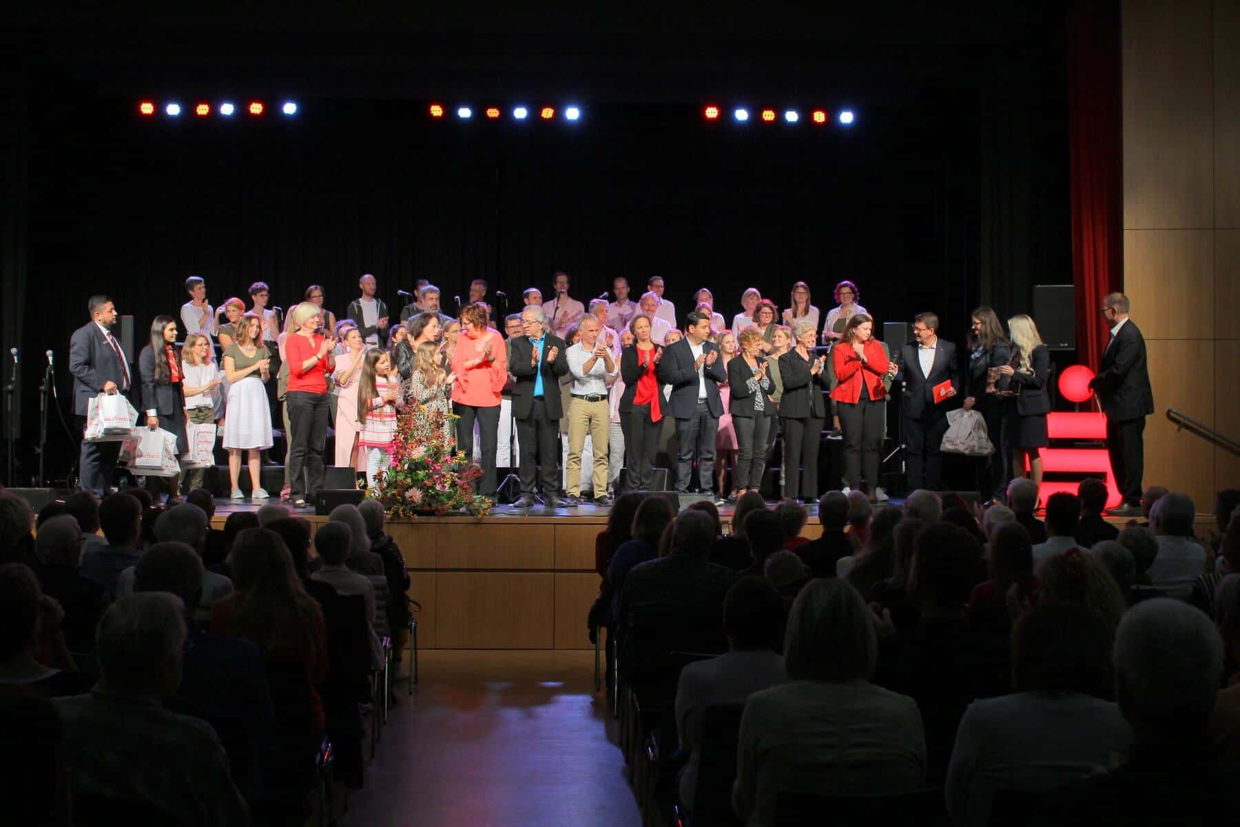 Sparkassen Chorfestival 2019: Vertreter der zwölf Chöre haben sich auf der Bühne versammelt, und warten gespannt, ob ihr Name aus dem Lostopf gezogen wird.