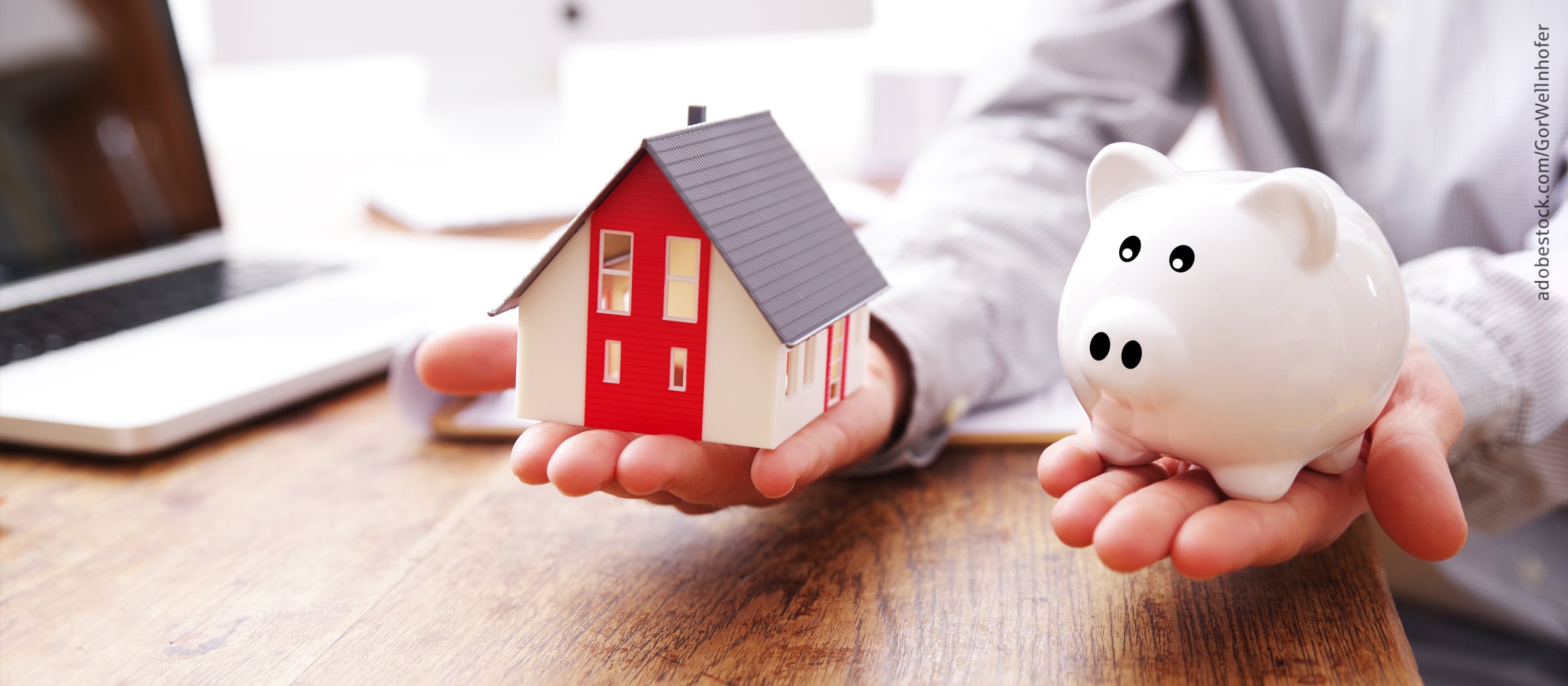 Ein Mann hält in einer Hand ein Modellhaus und in der anderen ein Sparschwein in der Waage